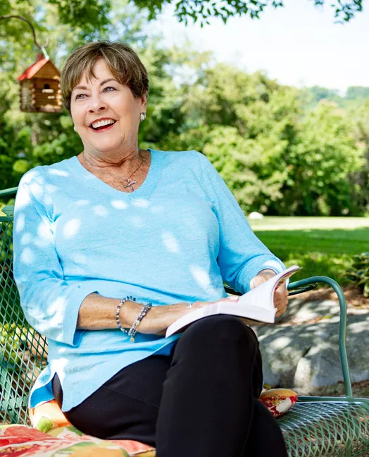 Shelia sitting on a park bench, reading a book on a beautiful sunny day